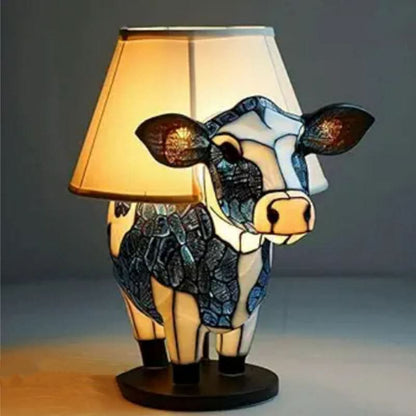 Cow lamp with blue and white glass body standing on a round dark base, fitted with a cream fabric lampshade. 12