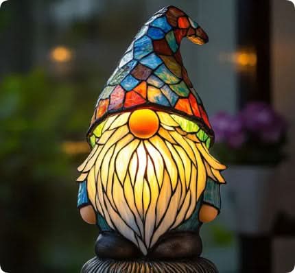 Garden gnome lamp with a blue and orange glass hat and long glowing white beard, shown beside blurred plants. 13