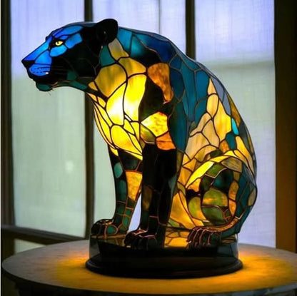Seated panther lamp in blue, green and yellow glass on an oval base, placed in front of a window. 16