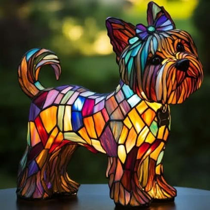 Small dog-shaped lamp with a bow in its topknot, a curled tail and a colourful mosaic body, seen from the side on a dark table. 27