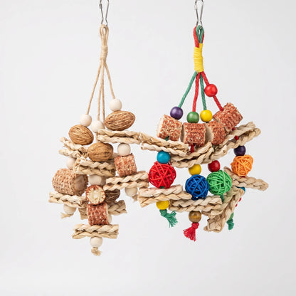 Two hanging bird toys against a plain backdrop: one natural, with nuts, wooden beads and woven grass, the other colourful with rattan balls. 1