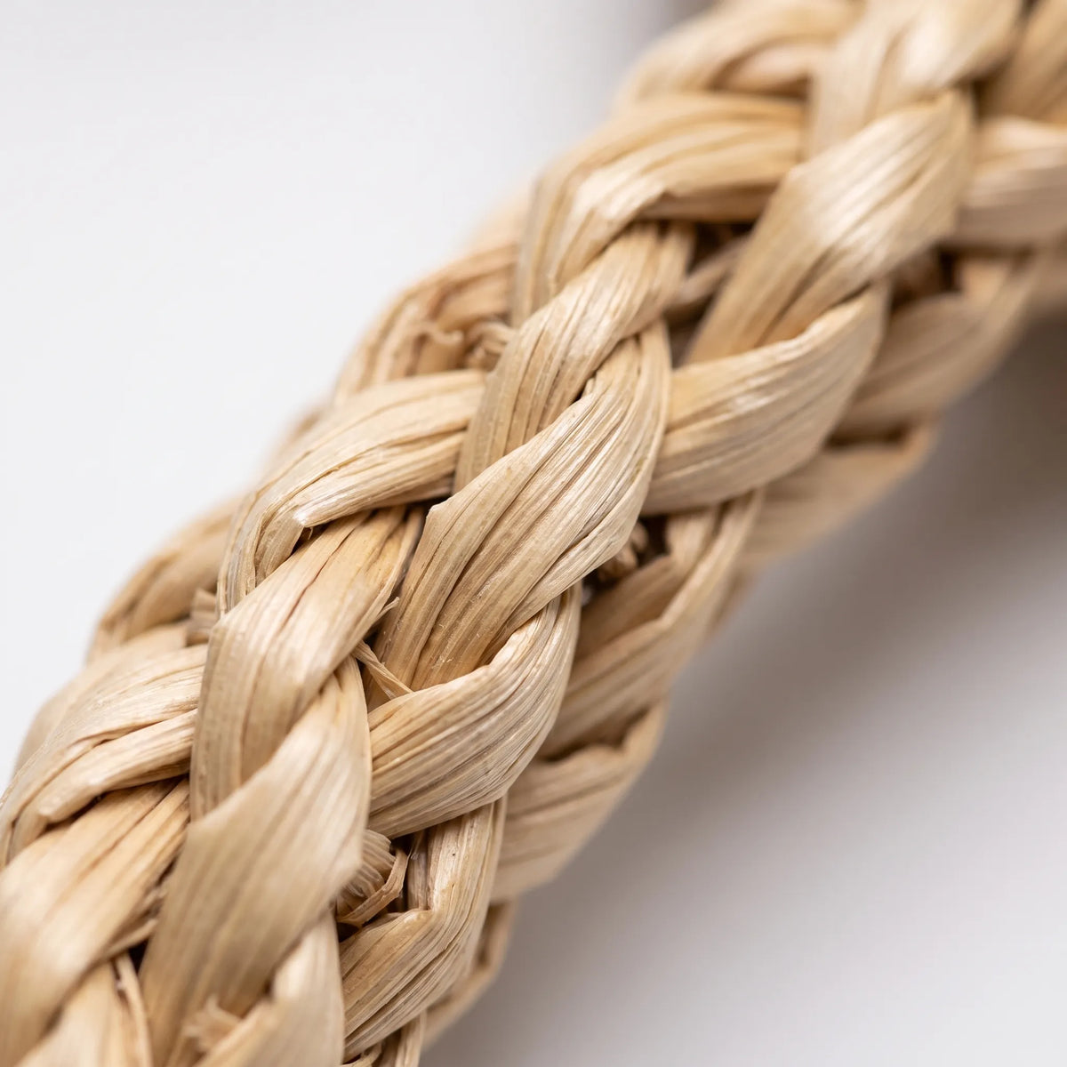 Close-up of braided, pale natural grass strands from the toy, showing the plaited texture against a white background. 3