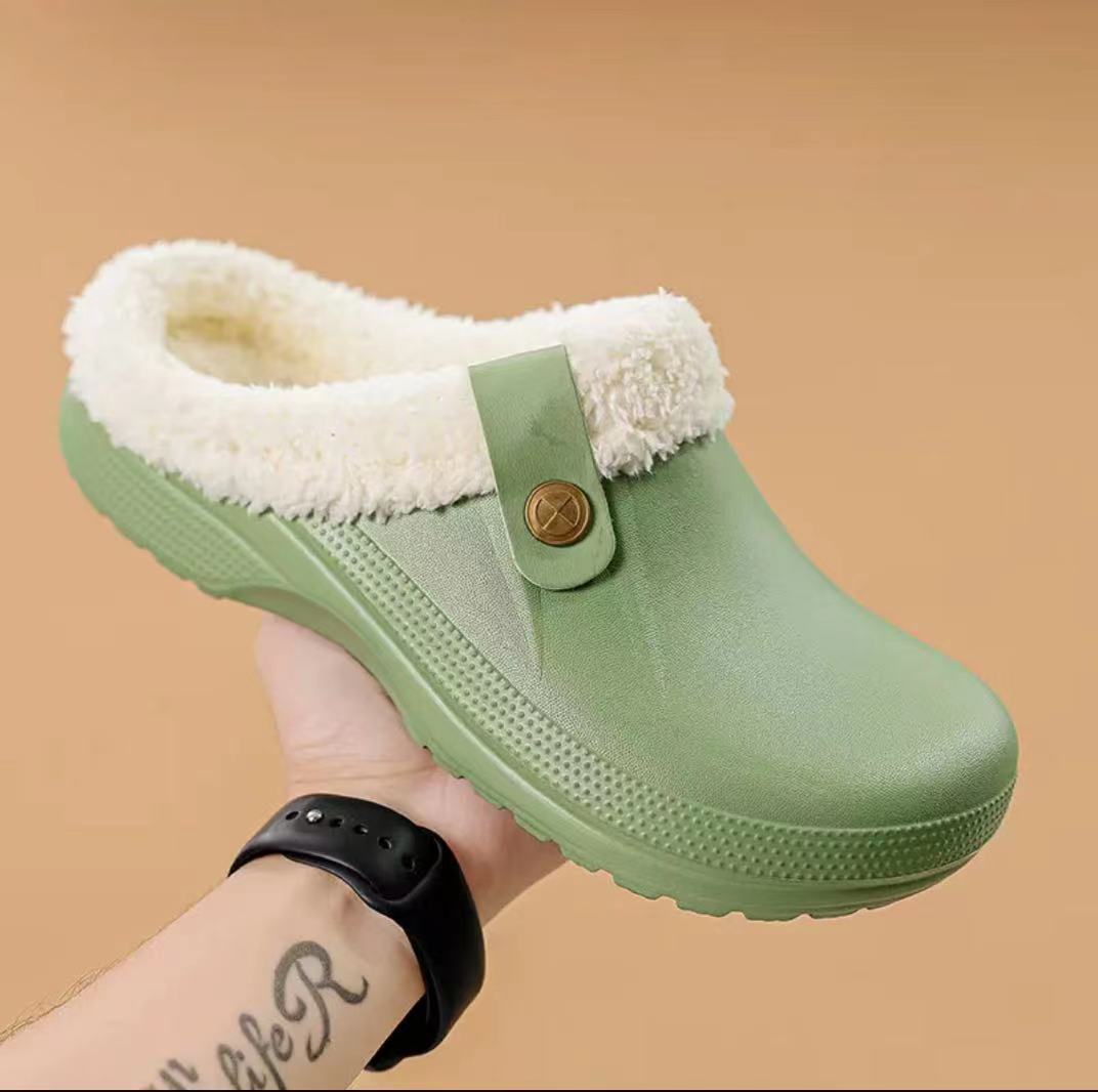 Hand holding a pale green clog with cream faux fur lining against a tan background 13