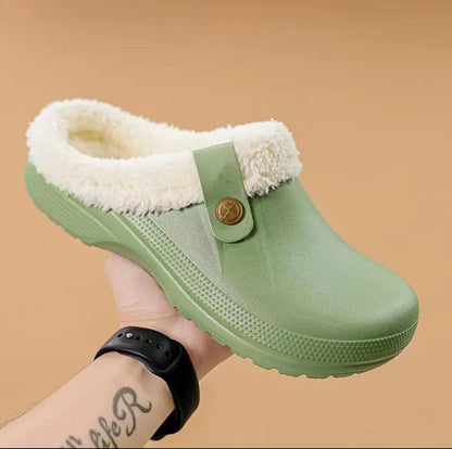 Hand holding a pale green clog with cream faux fur lining against a tan background 13