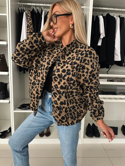 Close three-quarter view of a woman in the brown and black leopard print bomber shacket, buttoned over a black top with jeans, hand raised to her face. 1