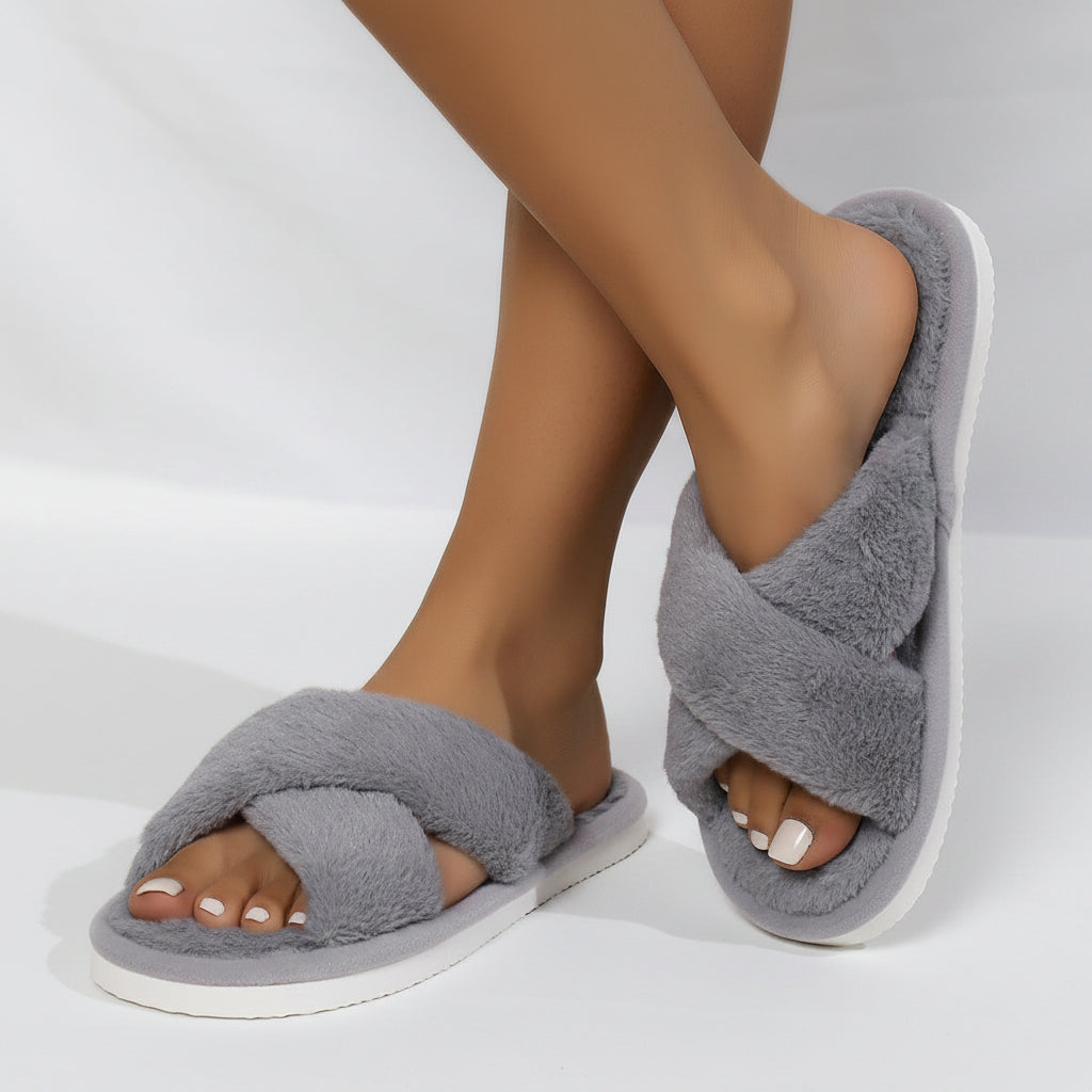 Grey plush crossover-strap slippers worn by a model, seen from the side with white soles and open toes. 5