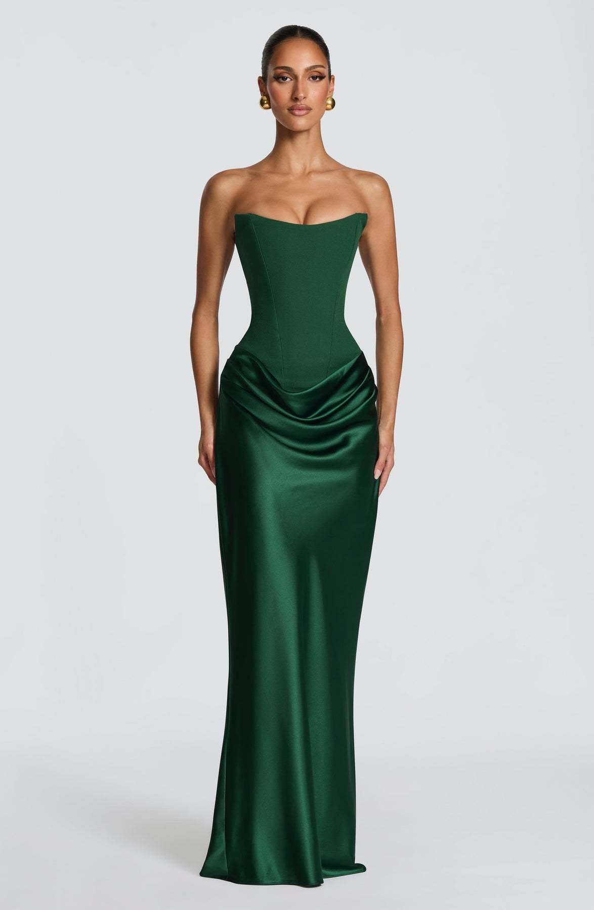Model facing forward in a strapless emerald green corset maxi dress with draped satin hip 1