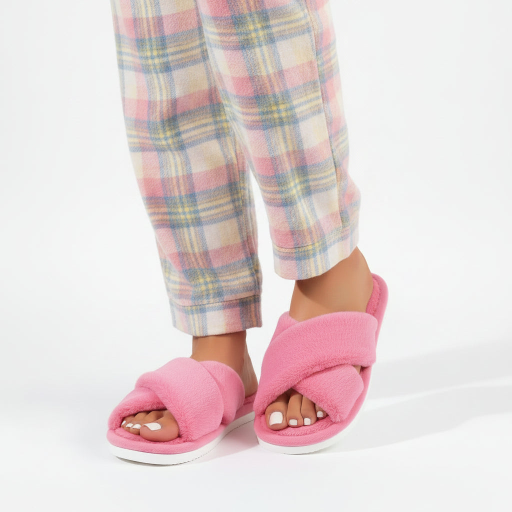 Worn by a model, pink plush crossover-strap slippers with white soles, paired with pastel plaid pyjama trousers. 2