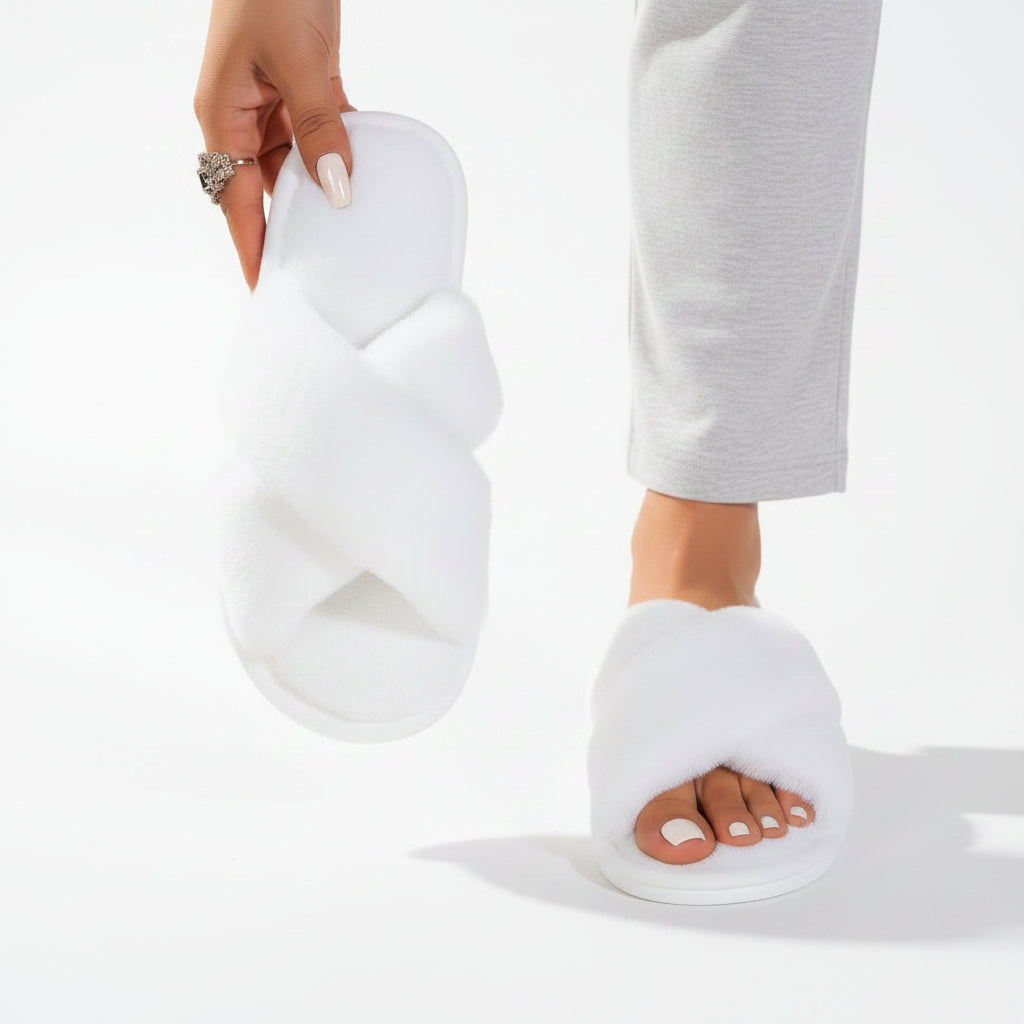 White fluffy crossover slippers, one worn with grey trousers and the other held up to show its soft footbed. 6