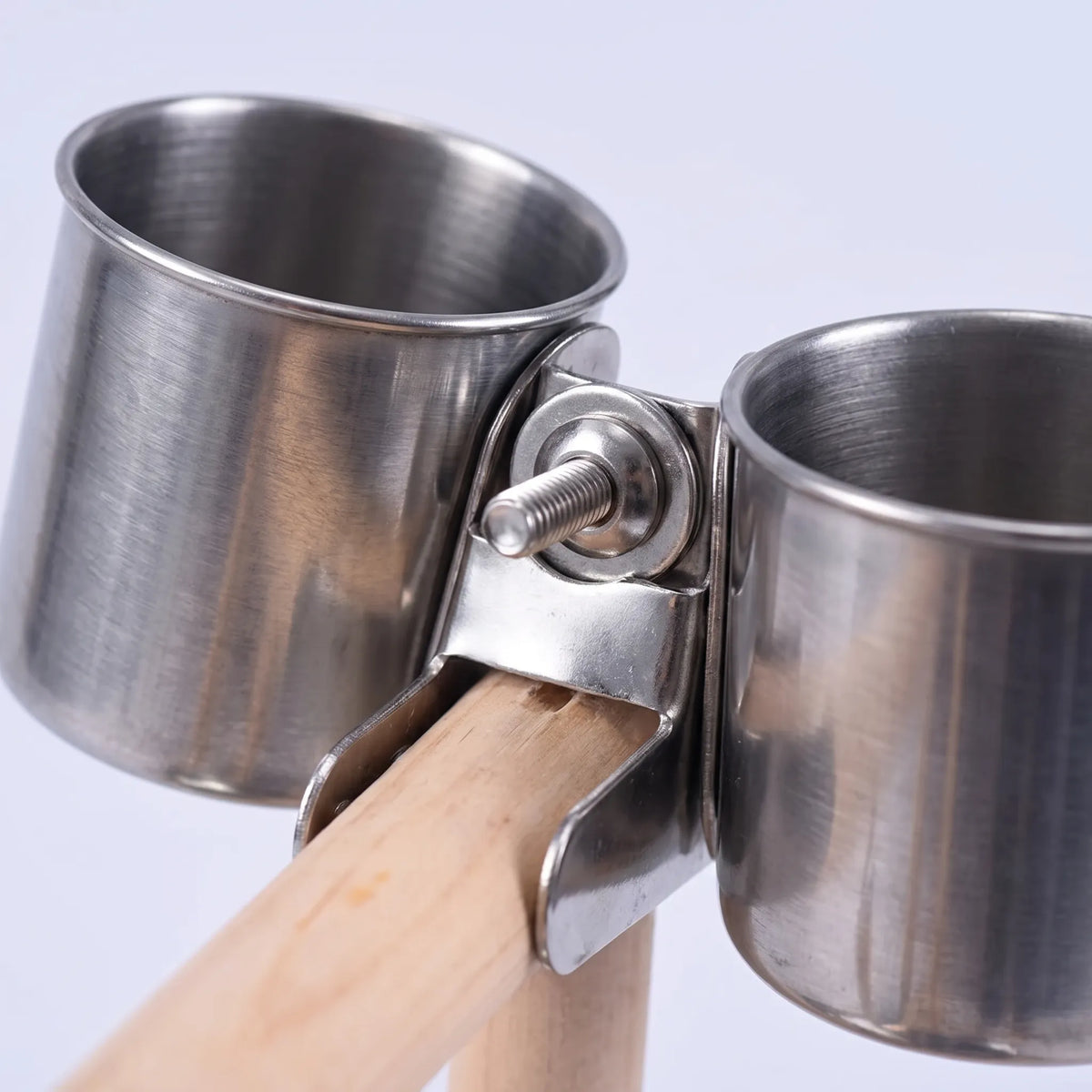 Close-up of the two stainless steel cups held by a metal clamp with a screw on the wooden perch. 4