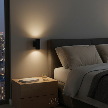 Black wall light casting a warm glow beside a bed, with a wooden bedside table holding a book and a glass of water. 7