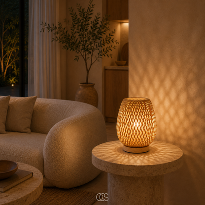 Woven bamboo lamp glowing on a round stone side table beside a curved cream sofa and a potted olive tree. 4