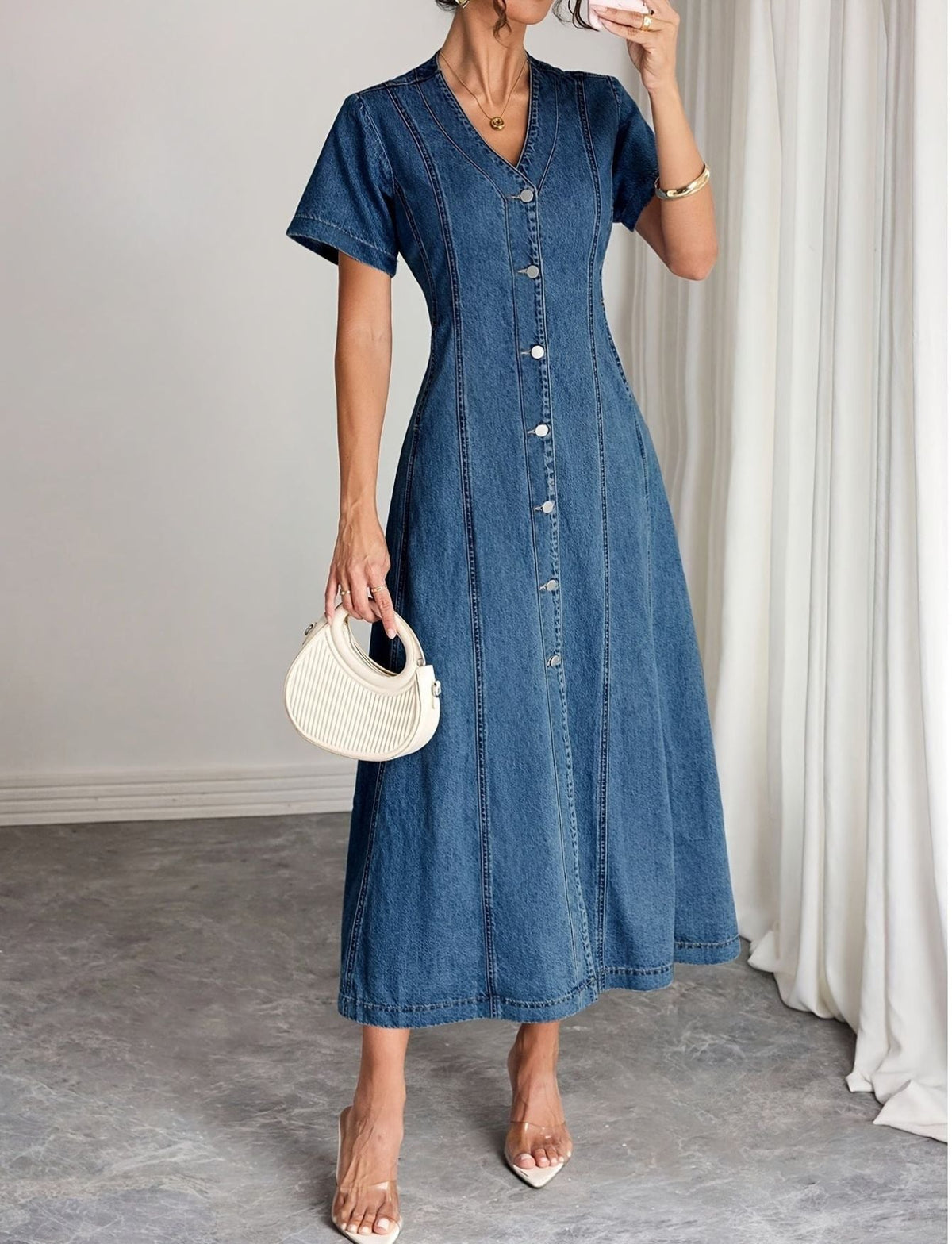 Model in the button-front midi dress holding a cream ribbed handbag, one hand raised near her face 1