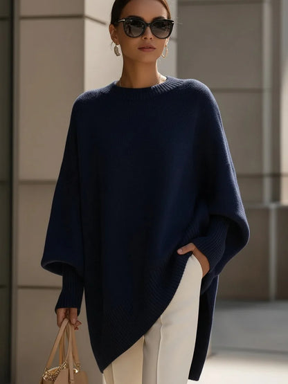 Model wearing the navy blue jumper with sunglasses, cream trousers and a beige handbag, one hand in a pocket. 8