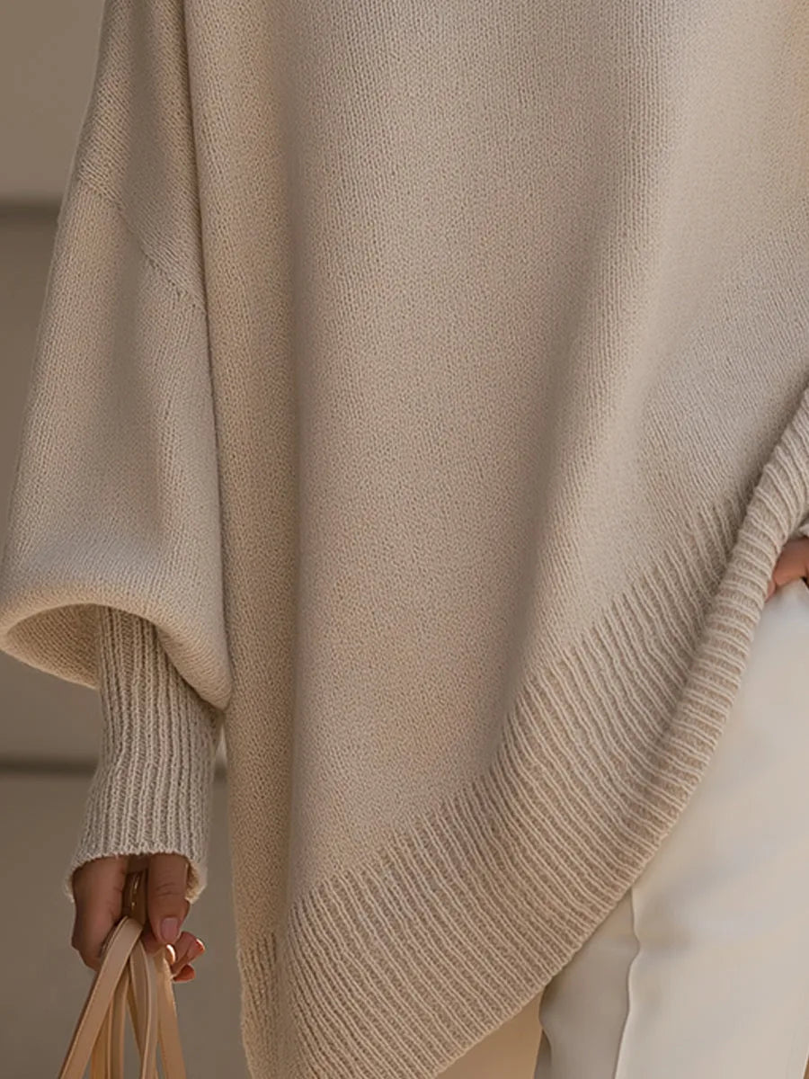 Close-up of the cream jumper's ribbed cuff and slanted ribbed hem, with the model holding a beige bag. 3