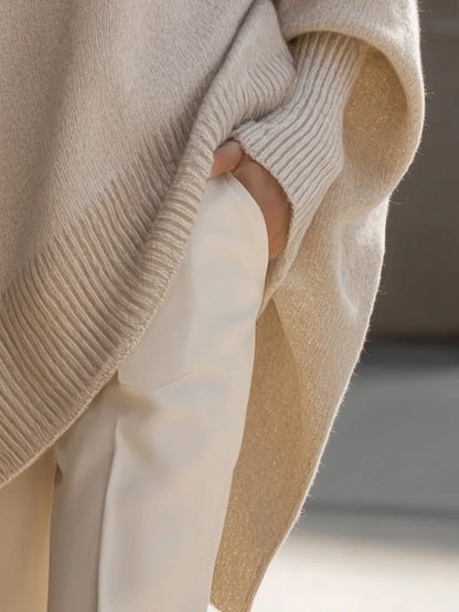 Detail of the cream jumper's side slit and ribbed hem, with a hand tucked into a white trouser pocket. 5