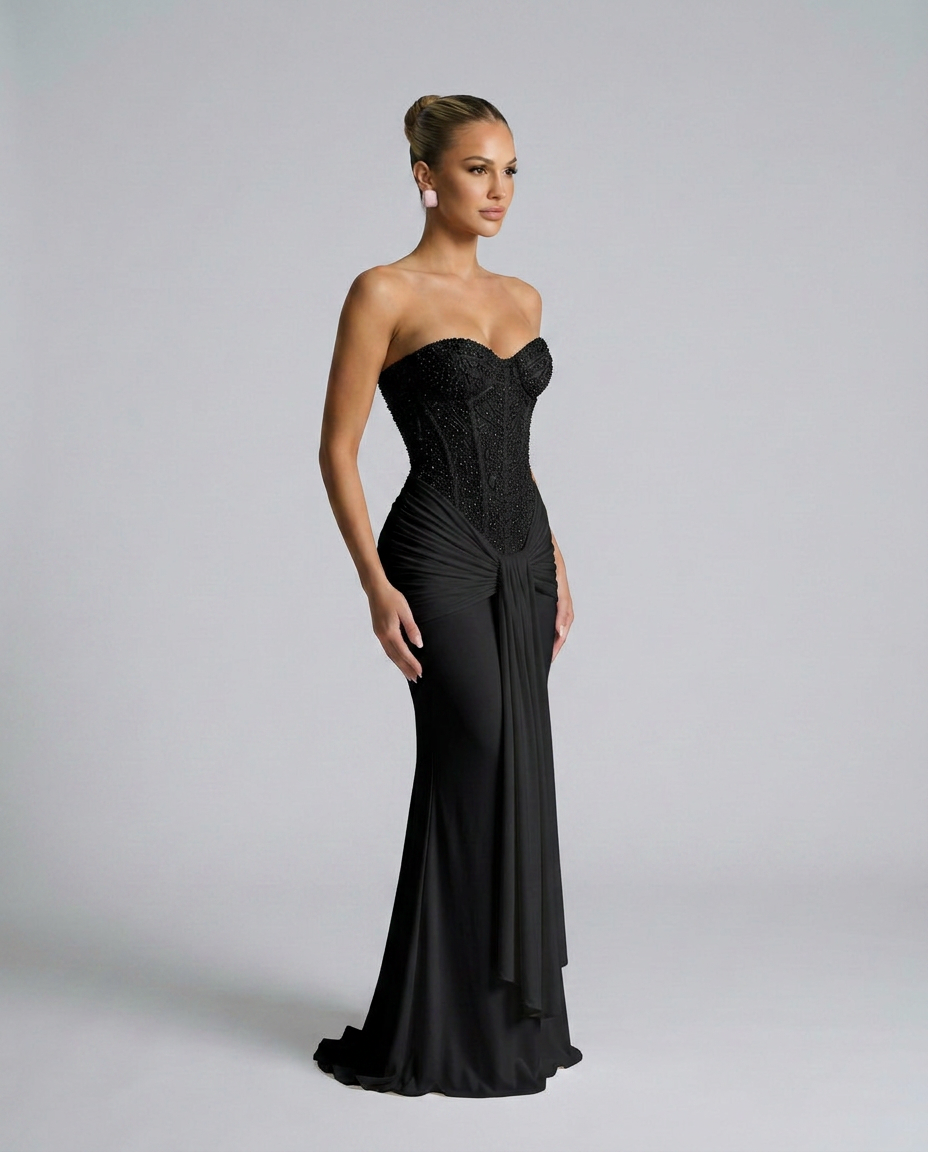 Black beaded corset maxi dress worn by a model turned in three-quarter view, showing the draped panel 2