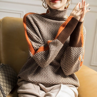 Woman seated on a mustard sofa in the brown herringbone jumper, hands together, showing orange side stripes and brown cuffs. 3