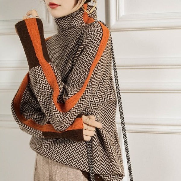Close-up of the herringbone jumper with orange sleeve stripes and brown cuffs, worn with a hand raised and a chain bag. 2