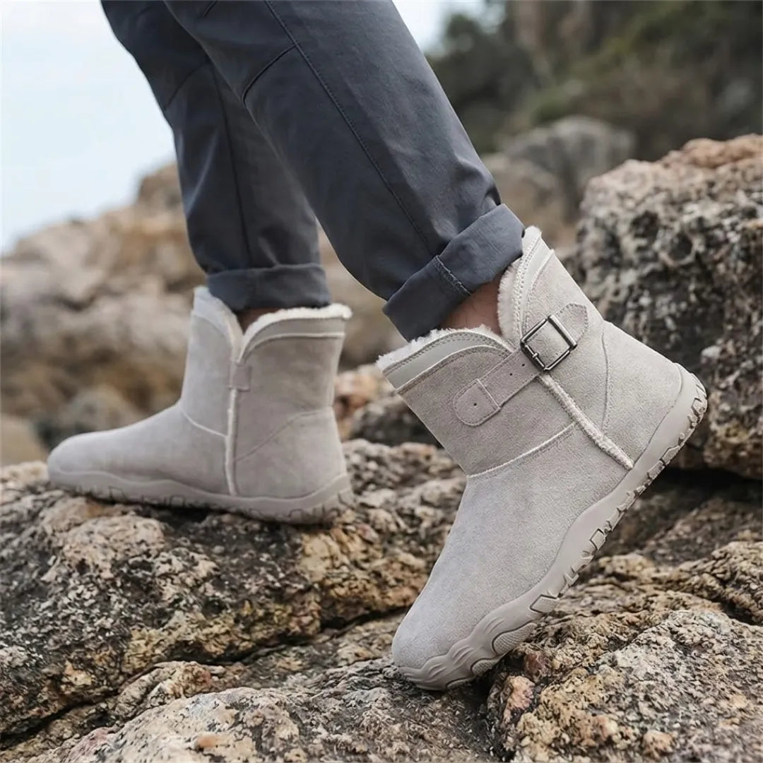 Model in rolled-up dark trousers wearing light grey fleece-lined boots while stepping across coastal rocks 29