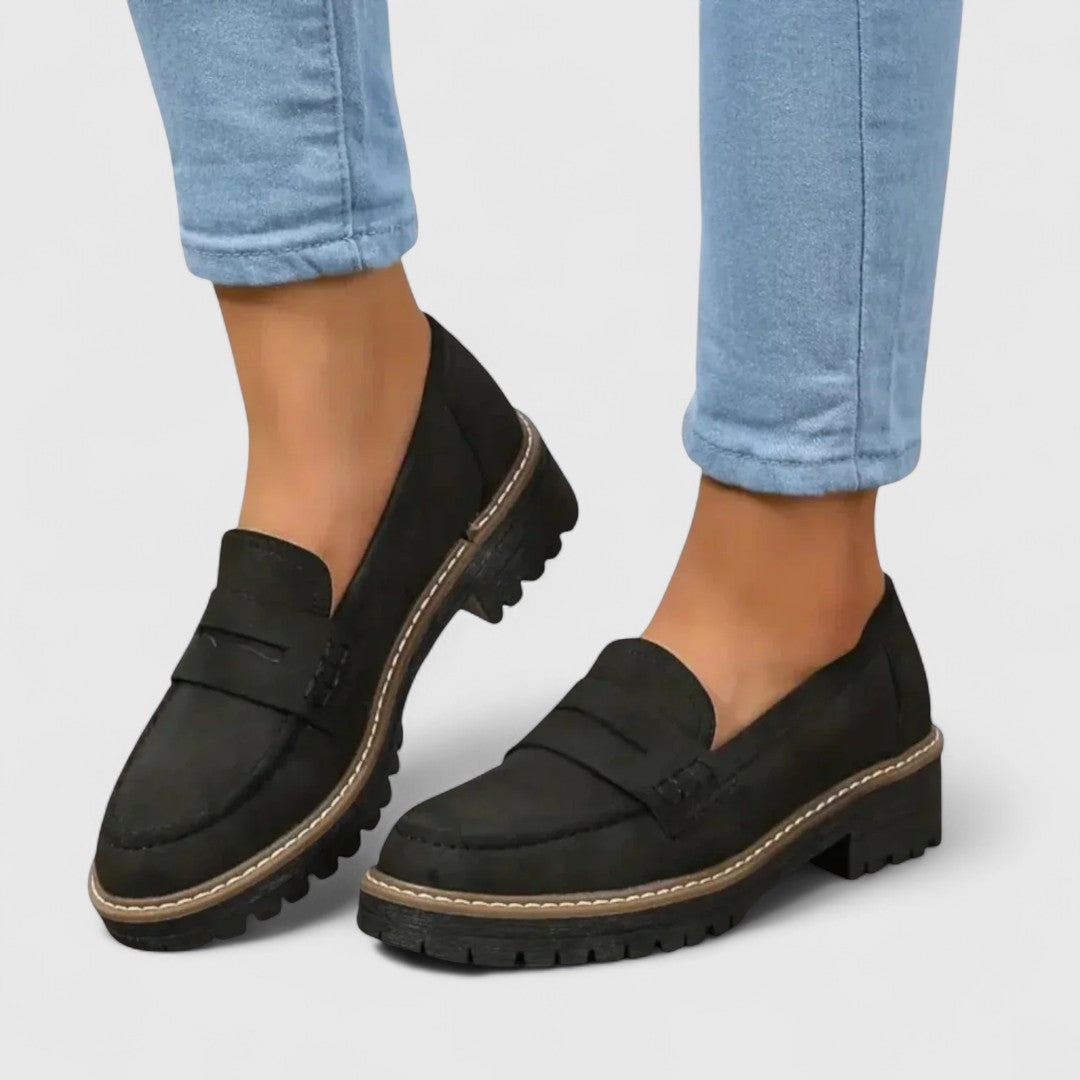 Black suede-look loafers with contrast stitching, worn with light blue jeans, seen from a three-quarter angle 1