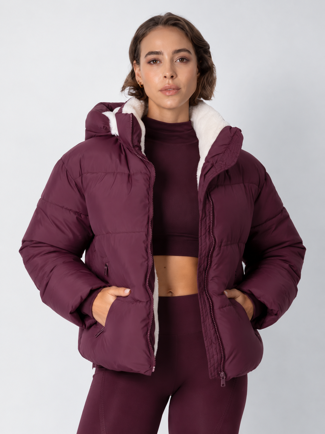 Model wears the deep burgundy puffer jacket open over a matching crop top, cream fleece lining showing 16