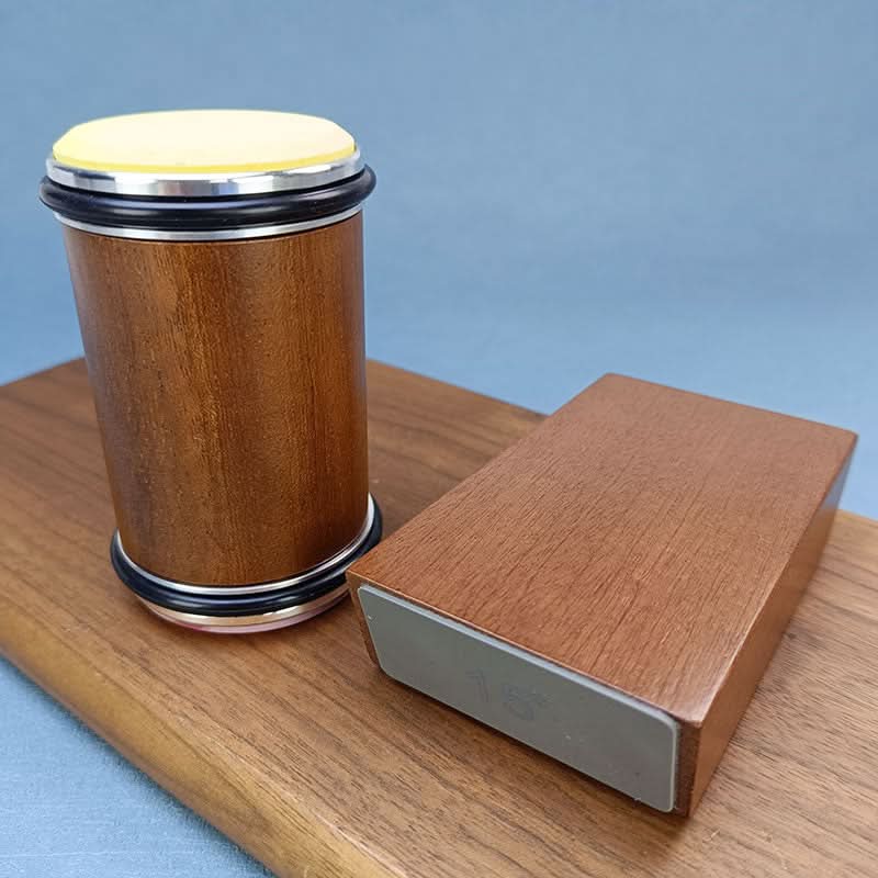 Wooden roller standing upright beside its angle block on a wooden board, with a pale yellow disc on top and black rubber rings. 5
