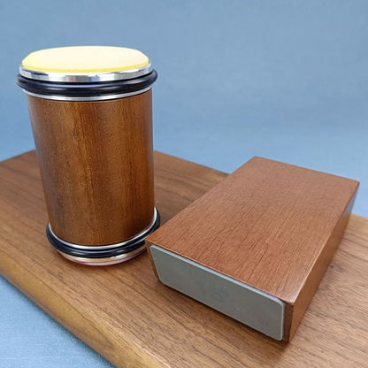 Wooden roller standing upright beside its angle block on a wooden board, with a pale yellow disc on top and black rubber rings. 5
