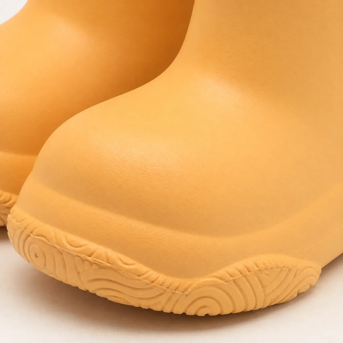 Close-up of the rounded toe and swirl-patterned sole of an orange welly, showing the smooth moulded finish. 6