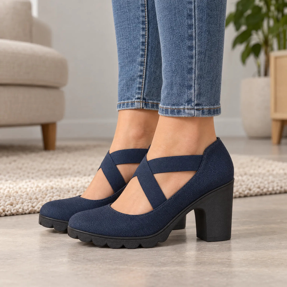 Close side view of navy block heels with crossed elastic straps and chunky treaded soles, worn with cropped jeans indoors. 2