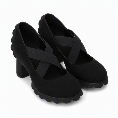 Pair of black suede-look block heel Mary Janes with crossed elastic straps and scalloped sole edges, shown from the front on white. 8
