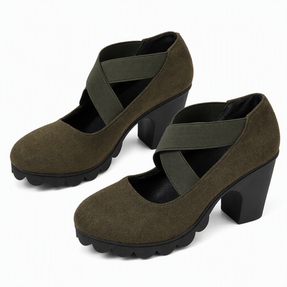 Pair of olive green suede-look block heel Mary Janes with crossed green elastic straps and black scalloped soles on white. 10