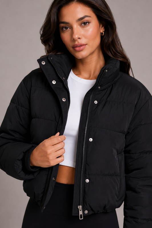 Close-up of the black quilted puffer jacket worn open over a white crop top, showing the stand collar, zip and press studs. 1