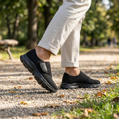 All-black mesh shoes worn by a walker in light trousers on a gravel path in a sunny park. 11