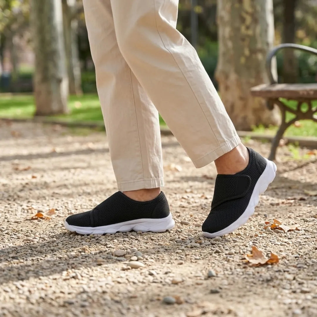 Black mesh shoes with white soles worn by a walker in beige trousers on gravel beside a park bench. 20