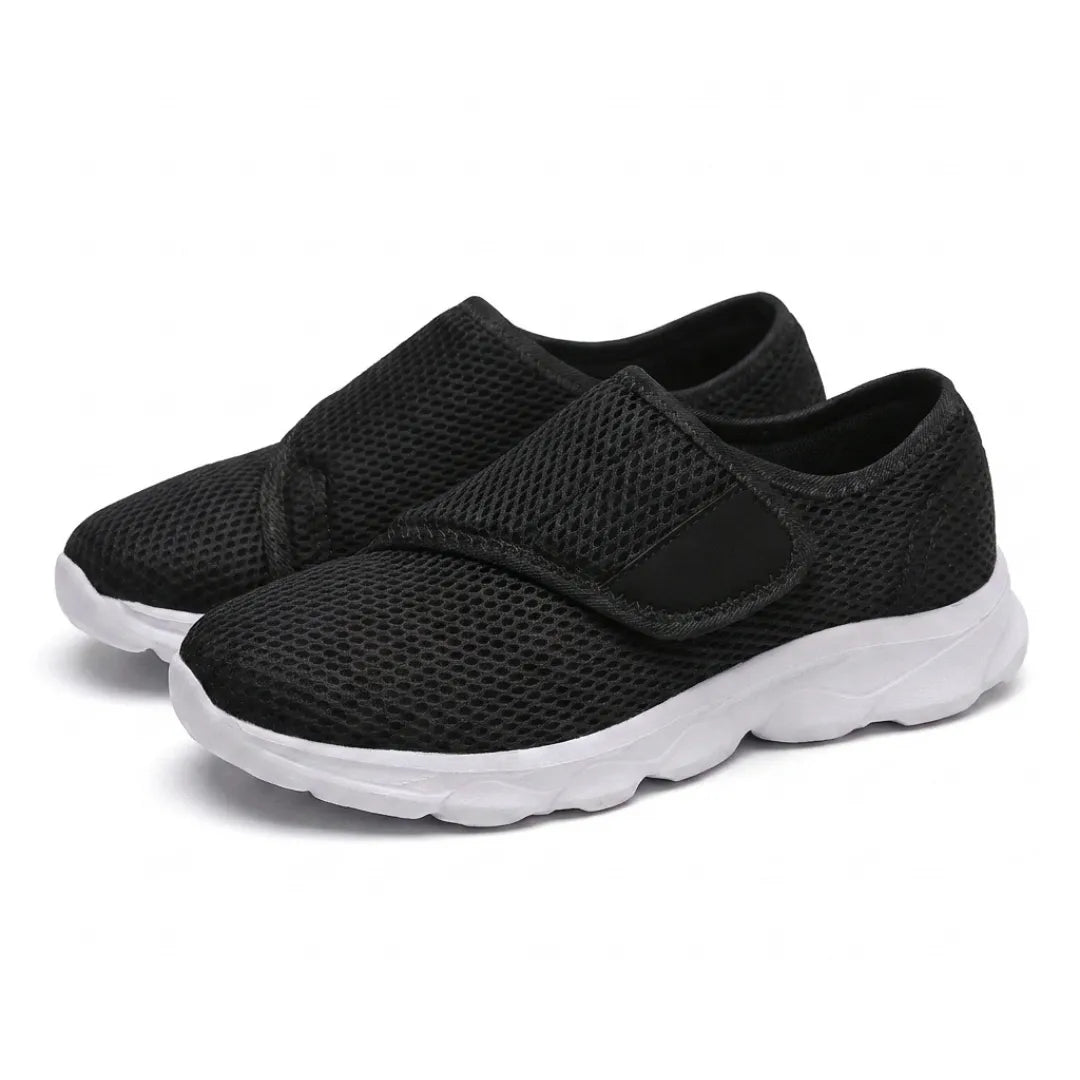 Pair of black mesh shoes with white soles and hook-and-loop straps, seen from the front three-quarter angle. 25