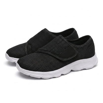 Pair of black mesh shoes with white soles and hook-and-loop straps, seen from the front three-quarter angle. 25