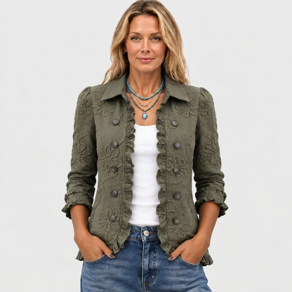 Model facing the camera in the olive green jacket with hands in jeans pockets, a white top and turquoise necklace. 2
