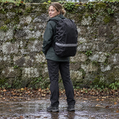 Woman in a dark green jacket looks over her shoulder, wearing a black rucksack with a rain-spotted cover and reflective band. 1