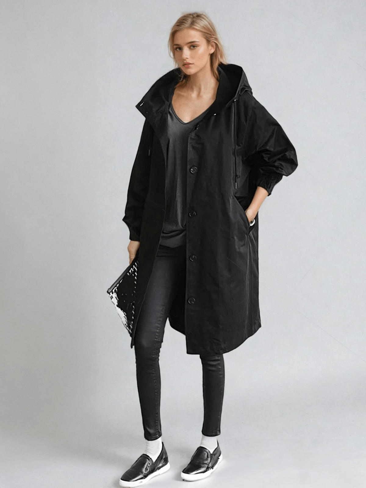 Full-length view of the long hooded coat in black on a model, styled with black jeans, trainers and a glossy clutch. 2
