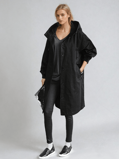 Full-length view of the long hooded coat in black on a model, styled with black jeans, trainers and a glossy clutch. 2