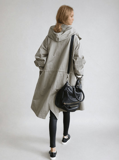 Back view of the long hooded coat in grey on a model, showing the hood, waist drawstring and a black shoulder bag. 4
