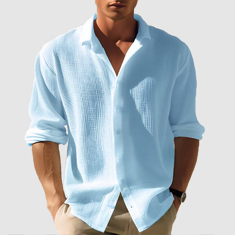 Model wearing the textured shirt in pale blue, sleeves rolled up, buttoned partway with a wide collar, hands in beige trouser pockets. 1