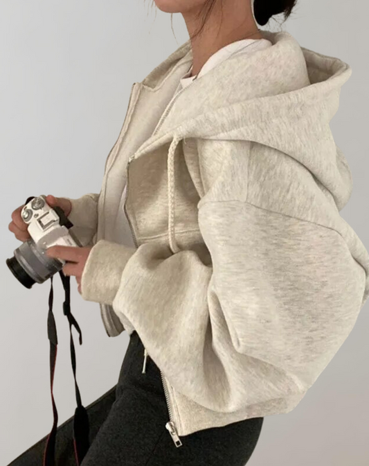 Side view of the pale marl hoodie worn by a model holding a camera, showing the voluminous sleeve and large hood. 2