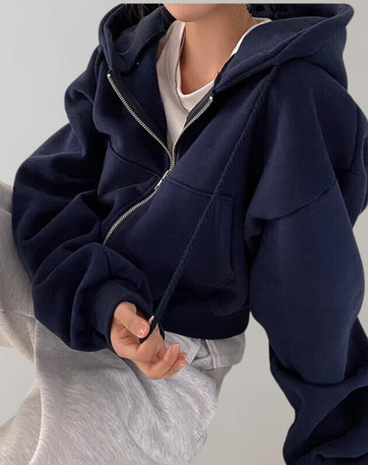 Navy zip-up hoodie worn open over a white top and light grey trousers, with the model holding a drawstring and gathered cuffs. 3
