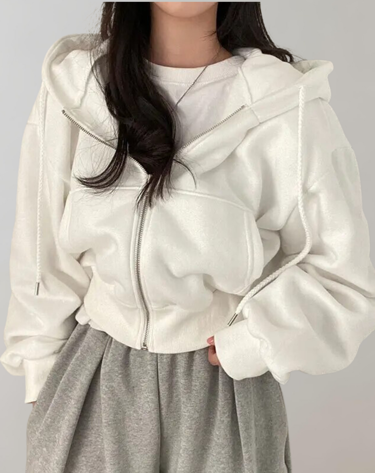 Model wearing the white zip-up hoodie half unzipped over a white tee and grey joggers, with braided drawstrings and ribbed hem. 1