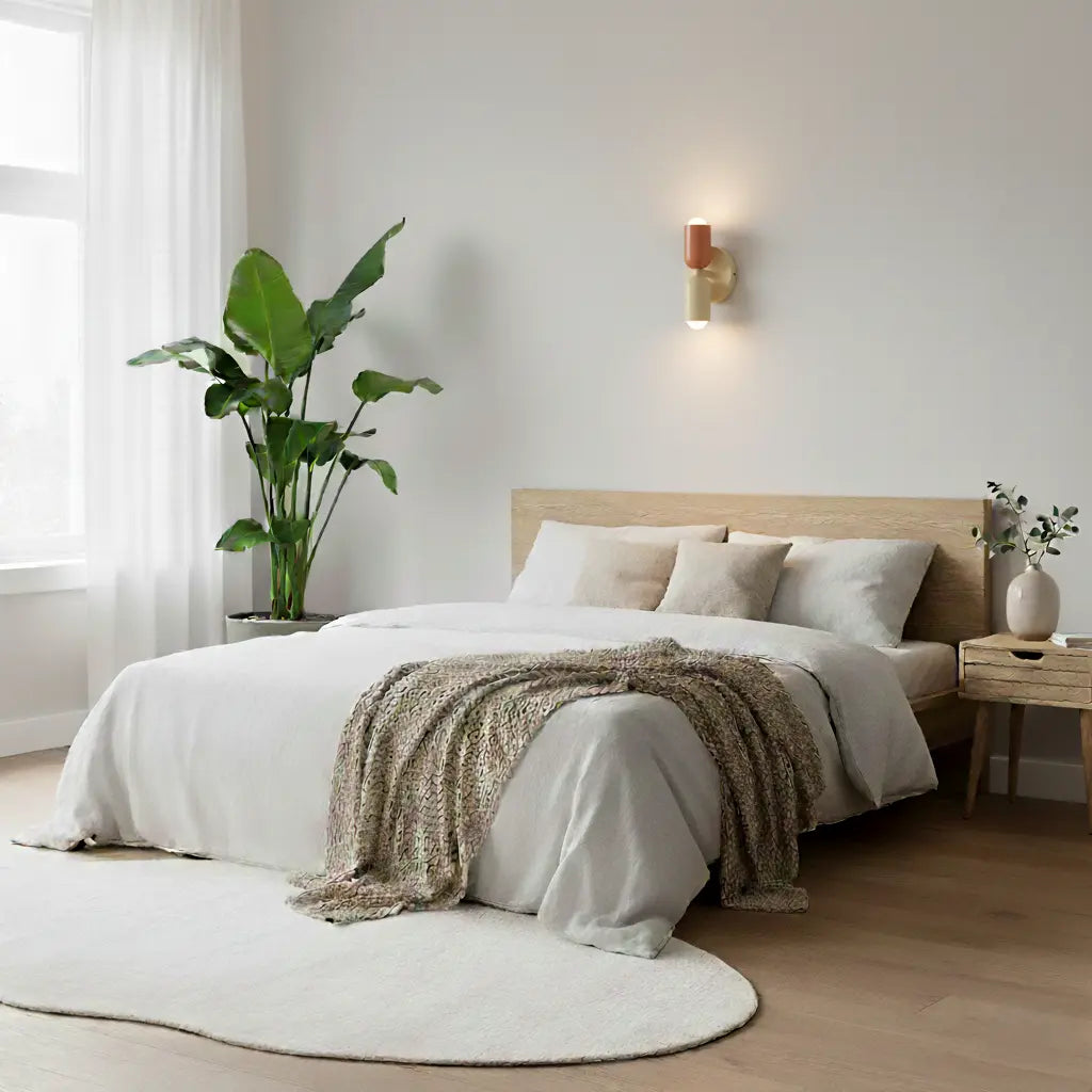Coral and cream wall lamp glowing above a calm bedroom with white linen, a wooden bed, a large plant and a round rug. 8
