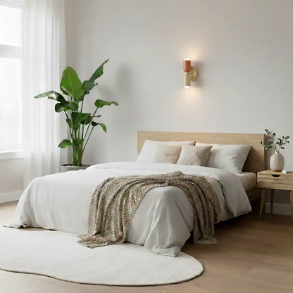 Coral and cream wall lamp glowing above a calm bedroom with white linen, a wooden bed, a large plant and a round rug. 8