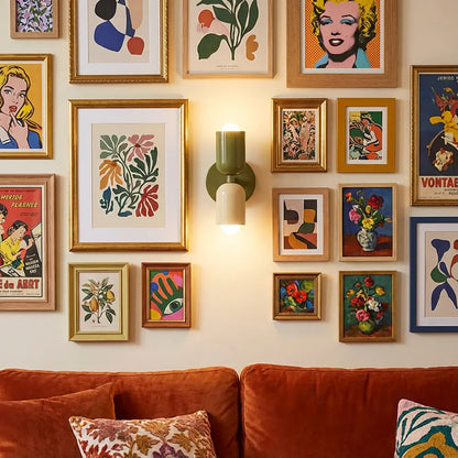 Olive green and cream wall lamp lit between a busy gallery wall of framed art, above a rust velvet sofa. 6