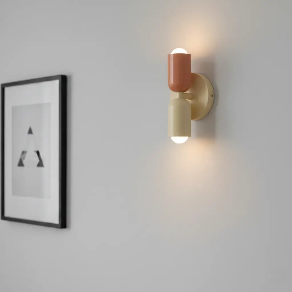 Coral and cream wall lamp lit on a pale grey wall, with a minimalist framed print beside it. 4